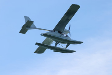 Seaplane (hydroplane or floatplane) flying in blue sky closeup. Cabin, wings propeller, engine, tail of plane are visible in details.