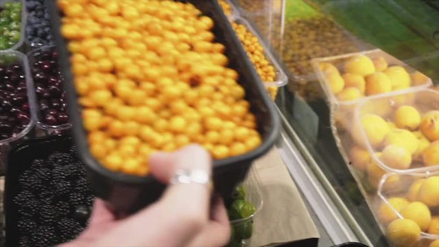 A woman chooses fresh sea buckthorn on the store counter in the supermarket. 
