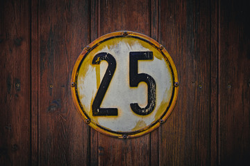 Old round shield with the number 25. Vintage, weathered metal sign saying twentyfive. Dark wooden background.