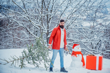 Fototapeta na wymiar Funny Santa man posing with axe and Christmas tree. Man with beard bears home a Christmas tree. Man lumberman with Christmas tree in winter park.