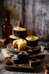 fresh baked homemade muffins with biscuit and cheesecake layers and almond petals on top stands wooden brown boards on grey table opposite concrete wall, selective focus