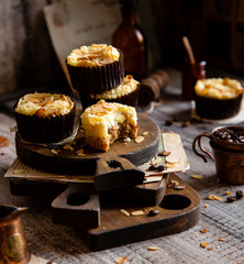 fresh baked homemade muffins with biscuit and cheesecake layers and almond petals on top stands wooden brown boards on grey table opposite concrete wall, selective focus