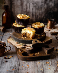 fresh baked homemade muffins with biscuit and cheesecake layers and almond petals on top stands wooden brown boards on grey table opposite concrete wall, selective focus