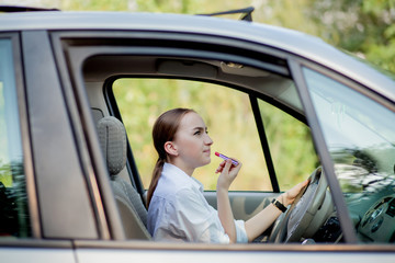 Picture of young businesswoman doing makeup while driving a car in the traffic jam