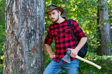 Naklejka na ściany i meble Lumberjack with ax in his hands. The Lumberjack working in a forest. Resting after hard work. Woodcutter with axe in the summer forest.