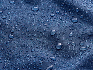 Rain water droplets on blue fiber waterproof fabric. Blue background.