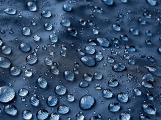 Rain water droplets on blue fiber waterproof fabric. Blue background.