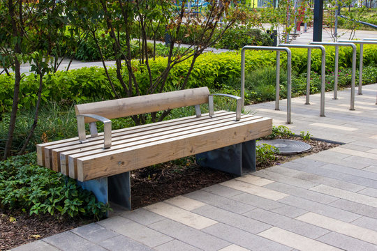 Macro photo of a modern wooden bench in the city park. City improvement, urban planning, public spaces. Wooden garden bench in the city on the background of nature