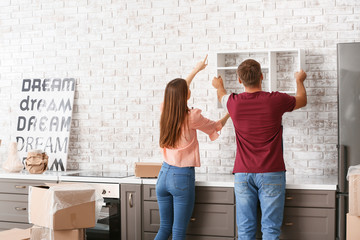Young couple hanging shelf on wall in their new house