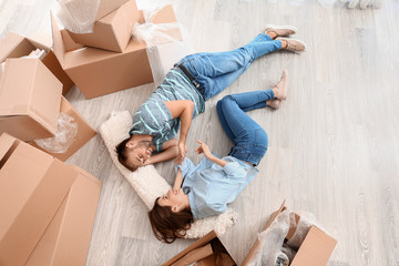 Happy young couple with belongings lying on floor in their new house