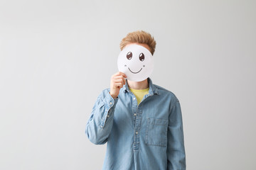Man hiding face behind emoticon on light background