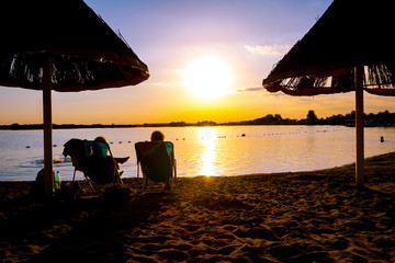 Silhouetted shot of sunset with couple, people by the beach