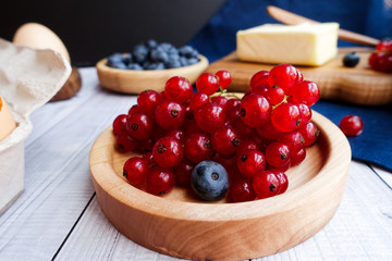 ingredients for baking lie on a light wooden background with a blue kitchen towel. butter, berries and wooden tools