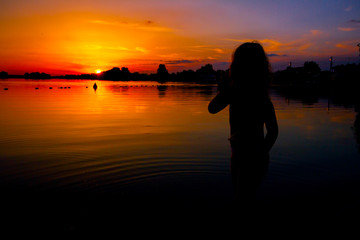 Fototapeta premium Silhouette of child by the lake and the orange sky in sunset