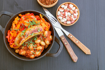 Stewed beans with vegetables and sausages. on black background.