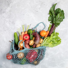 Top view of string bag with fresh farm vegetables on grey concrete background. 