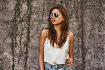Beautiful stylishly dressed girl posing over concrete background
