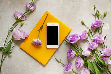 Modern mobile phone with flowers and notebook on grunge background