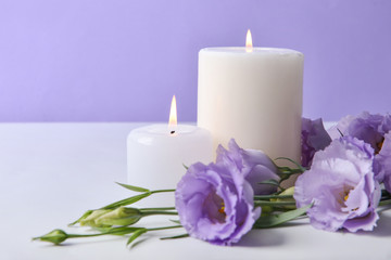 Burning candles with fresh flowers on table against color background