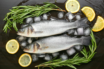 Fresh seabass fish, lemon, rosemary and ice cubes on dark background