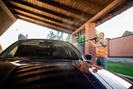 A Man In Orange Vest Washes His Car With A Large Head Of Water From A Karcher On Open Air. High Pressure Cleaning