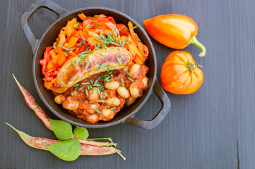 Stewed beans with vegetables and sausages. on black background.