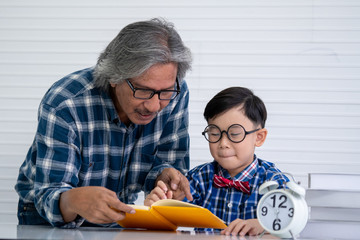 Happy asian senior retired grandfather teaching his grandson little boy do homework read and write at home. Love happy family generations relationship and people education concept.