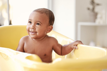 Little African-American baby washing in bathtub at home