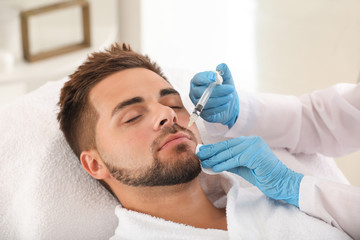 Handsome man receiving filler injection in beauty salon