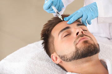 Handsome man receiving filler injection in beauty salon