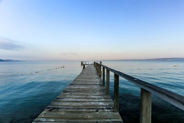 Fototapeta premium A brown wood pier horizon toward to the ocean and include shade of colors, blue and orange of sky and mountain in the background also.