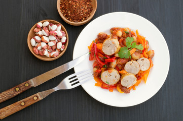 Stewed beans with vegetables and sausages. on black background.