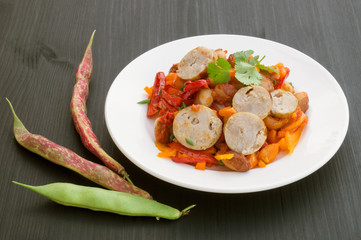 Stewed beans with vegetables and sausages. on black background.