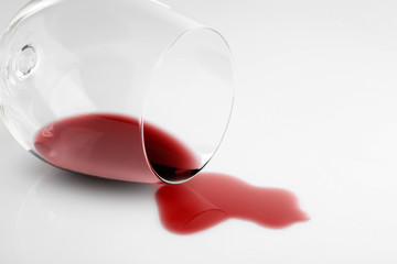 Transparent glass and spilled exquisite red wine on white background