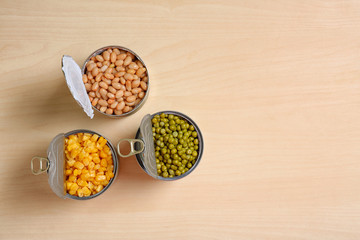 Open tin cans of conserved vegetables on wooden table, flat lay with space for text