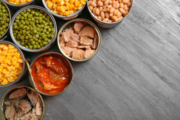 Open tin cans of conserved products on grey table, flat lay with space for text