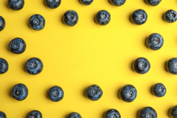 Frame of ripe blueberries on yellow background, flat lay with space for text