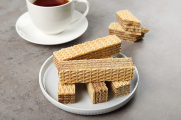 Plate of delicious wafers with cup of tea on grey stone background