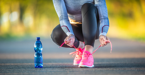 Woman runner tying shoelaces before jogging in autumn tree alley park. Sports female autumn outfit...