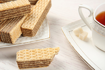 Plate of delicious wafers with cup of tea on white wooden background, closeup