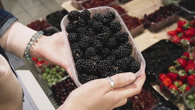 Vegetarian woman chooses blackberry on the store counter in the supermarket. 