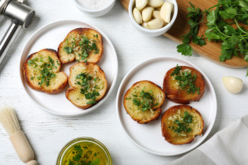 Slices of toasted bread with garlic and herb on white wooden table, flat lay