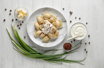 Delicious cooked dumplings with sour cream on white wooden table, flat lay