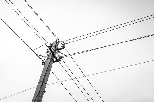Low Angle Black and White Image of a Concrete Utility Power, Electricity Pole with Insulators and Cables.