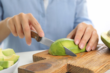 Woman cutting ripe avocado at table, closeup