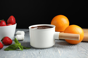 Fondue pot with chocolate, fruits and marshmallow on grey wooden table