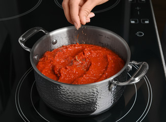Woman cooking delicious tomato sauce in pan on stove, closeup