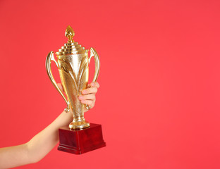 Child holding golden winning cup on red background, closeup. Space for text