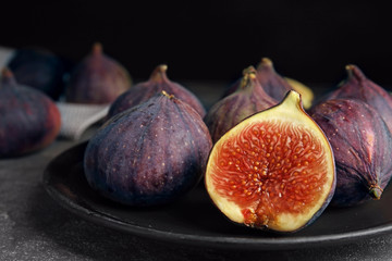 Plate with ripe figs on grey table against dark background, closeup