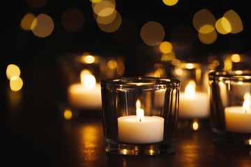 Burning candle on table against blurred background. Funeral symbol
